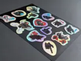 Holographic sticker sheet at angle showing color-shift effect with cute designs - Sticker Sheet Printing